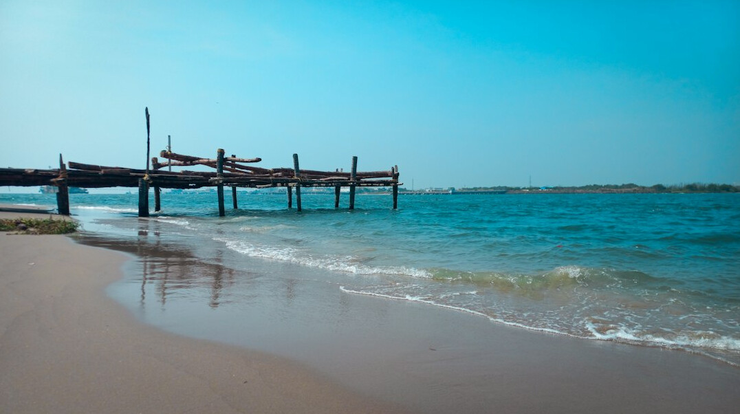 Quiet sandy beach with calm blue sea and a wooden pier